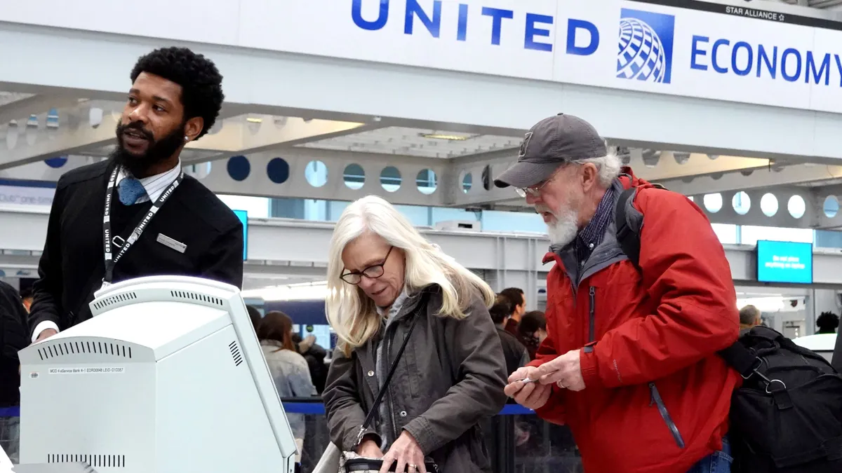 A United Airlines employee helps two passengers check in for their flight.