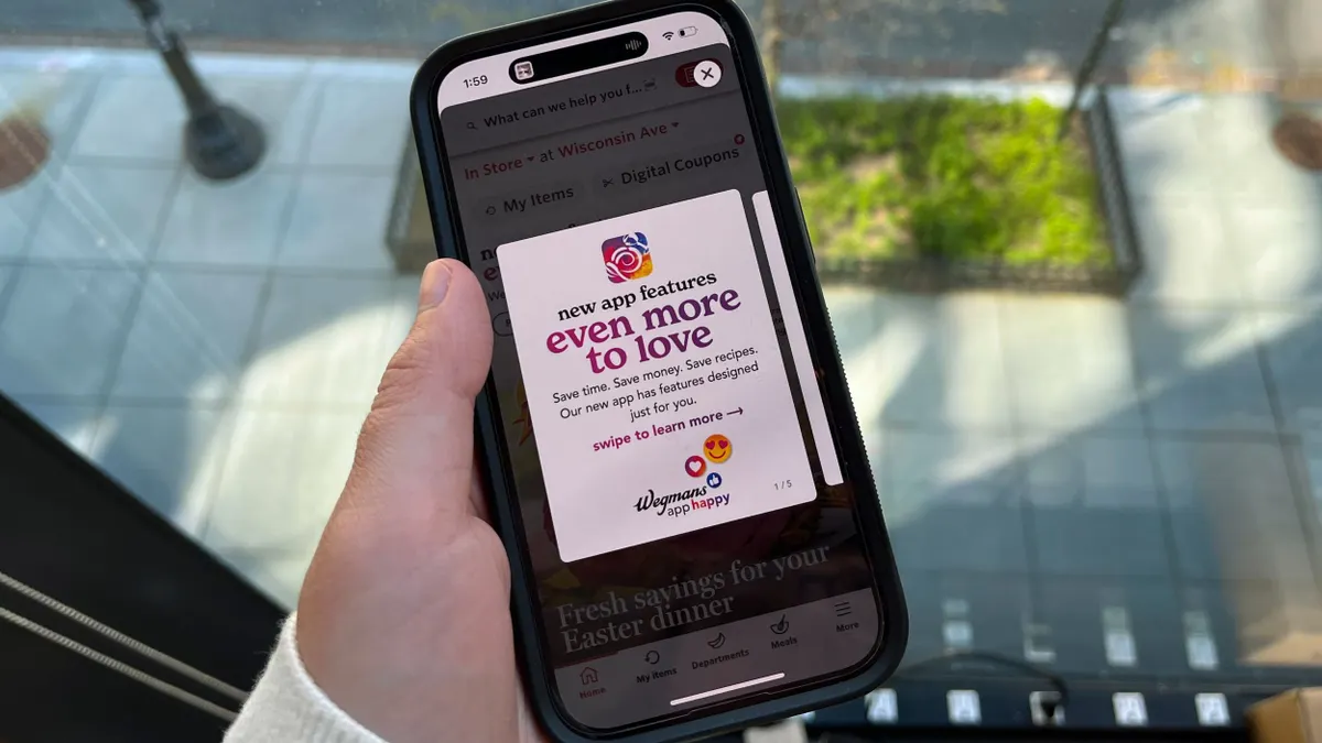 A hand holds an iPhone that displays Wegmans' updated app, and the screen reads, "New app features, even more to love."